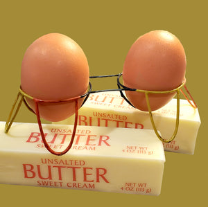 two eggs nestled in a wire egg holder sitting atop butter sticks 